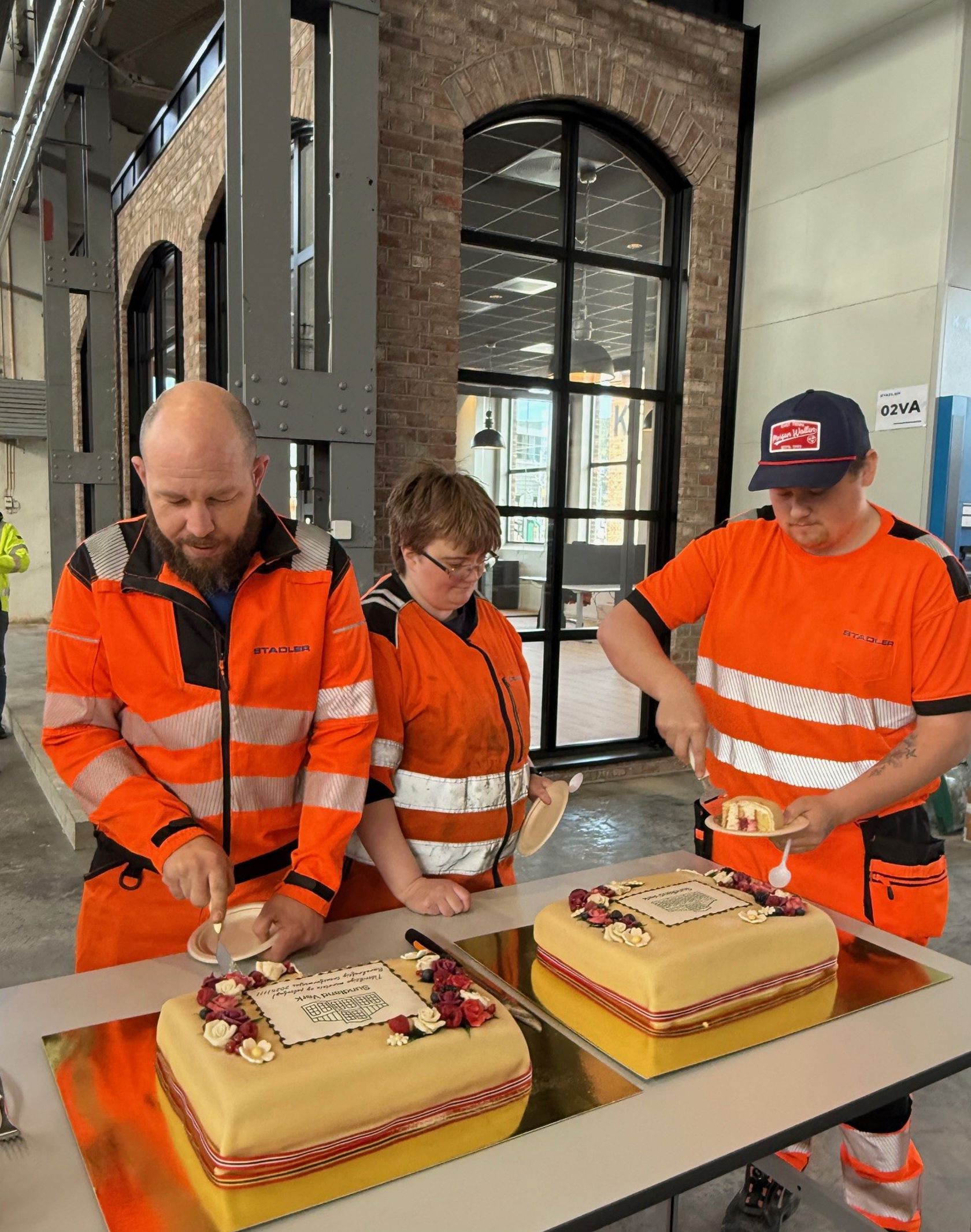 Tre mennesker i oransje arbeidsklær skjærer opp kake. 