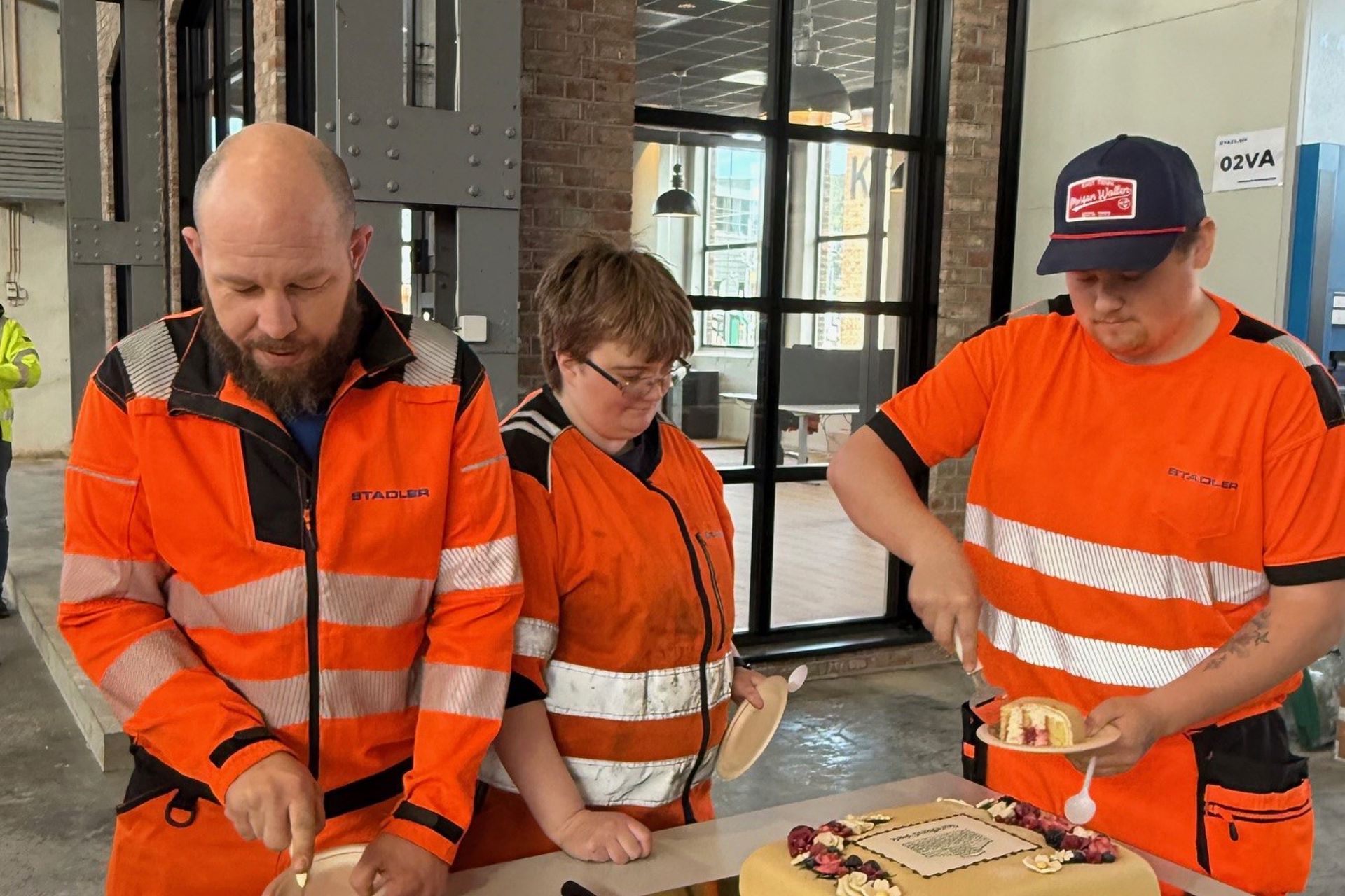 Tre mennesker i oransje arbeidsklær skjærer opp kake.
