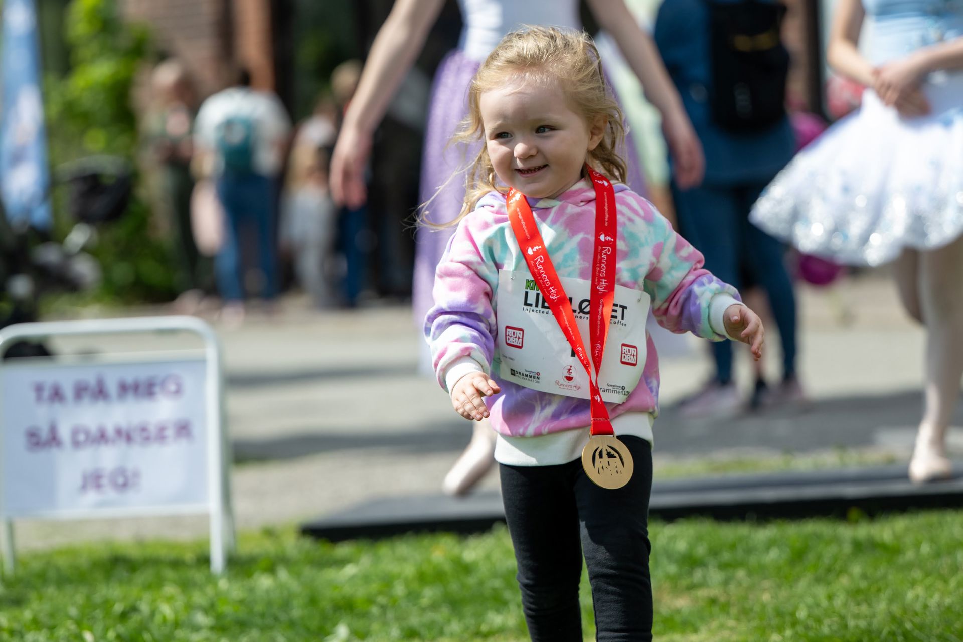 En liten jente med medalje rundt halsen og startnummer på magen går på gresset.